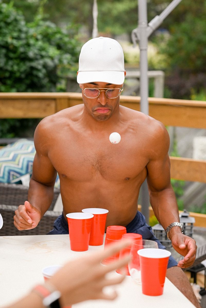 Shirtless host playing beer pong on a terrace
